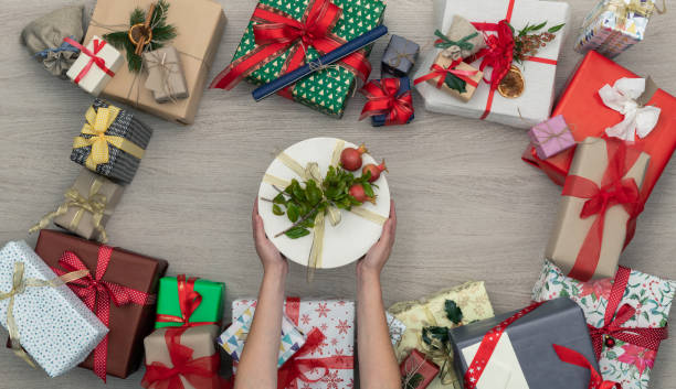 Hands with gift present box in vertical top view wooden table full of christmas or birthday gifts presents.Xmas winter holiday season party social media card background,portrait story. manos con regalo presente la caja en la vista superior vertical presenta mesa de madera llena de regalos de navidad o cumpleaños. fondo, historia del retrato de la tarjeta de navidad invierno vacaciones temporada partido sociales medios de comunicación