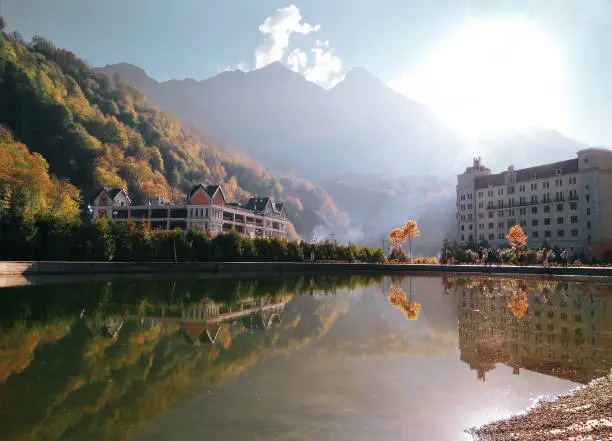 Panoramic scenic view of Rosa Khutor beach in Krasnaya polyana (Sochi, Russia). Water reflection of mountains and hotels in famous ski resort at summer autumn day