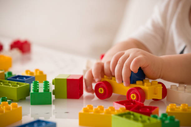 nahaufnahme der kinderhände spielen mit bunten kunststoffziegeln am tisch. kleinkind mit spaß und bauen aus hellen konstrukteur ziegel. frühes lernen.  streifenhintergrund. entwicklung von spielzeug - cube baby child block stock-fotos und bilder