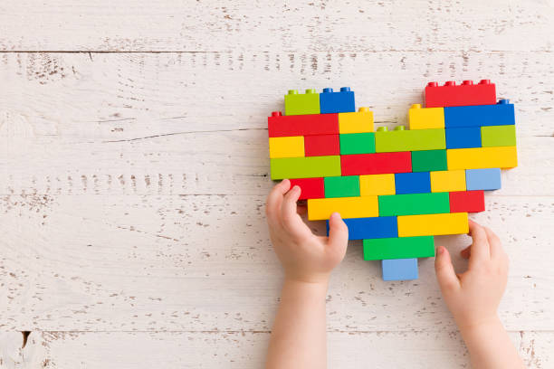 vista superior de las manos del niño jugando con el brillante corazón de ladrillos de plástico coloridos sobre la vieja mesa de madera. edificio de ladrillos de brillante constructor creativo. aprendizaje temprano. desarrollo de juguetes - cube baby child block fotografías e imágenes de stock