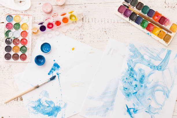 istock Top view on child's drawings and colorful paints and brushes. Creative ideas, creativity andearly learning. Education concept. 1058909640