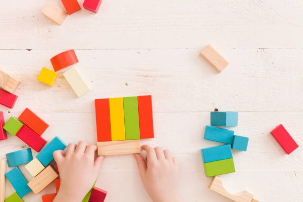 istock Top view on child's hands playing with colorful wooden bricks on the white table background.Kid building with geometric shapes. Learning and education concept. 1058909984