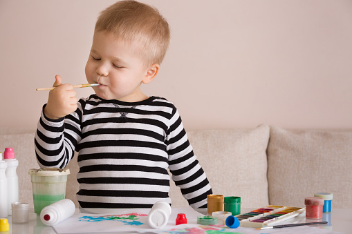 Portrait of cute toddler boy drawing at home with colorful paints and brush. Creative child having fun. Educational concept