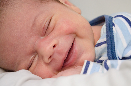 two weeks old newborn baby boy smilleing while sleeping close up