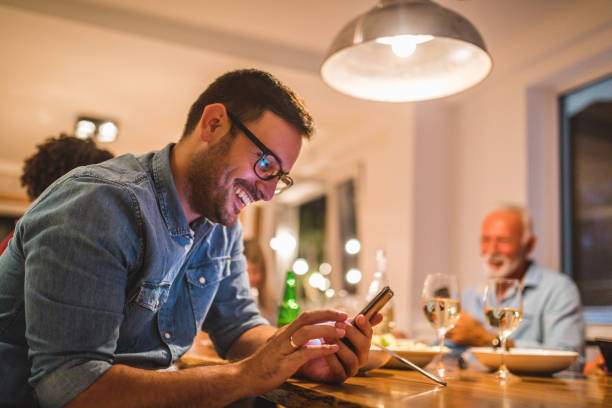 man holding a mobile phone while dining with family - gourmet enjoyment food freshness imagens e fotografias de stock