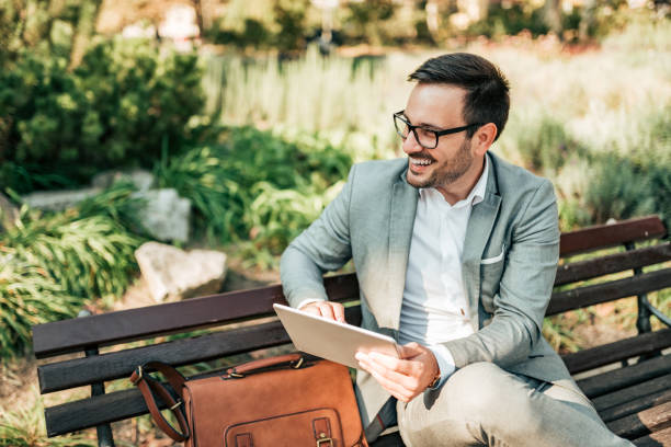 istock Handsome businessman sitting on a bench in the park using tablet. 1058944350