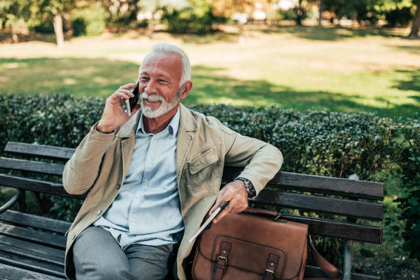 istock Smiling senior man talking on the phone while sitting on the bench in the park. 1058945332