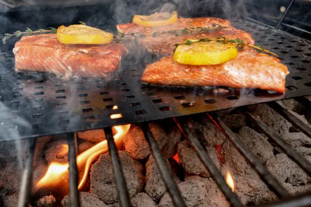 Appetizing salmon filets on a grill with flames and tarragon herbs and lemon on top