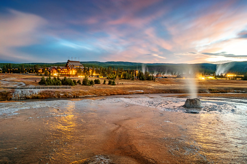 Stock photograph of a geyser cone and the landmark Old Faithful Inn in the Upper Geyser Basin, Yellowstone National Park on a cloudy, colorful evening