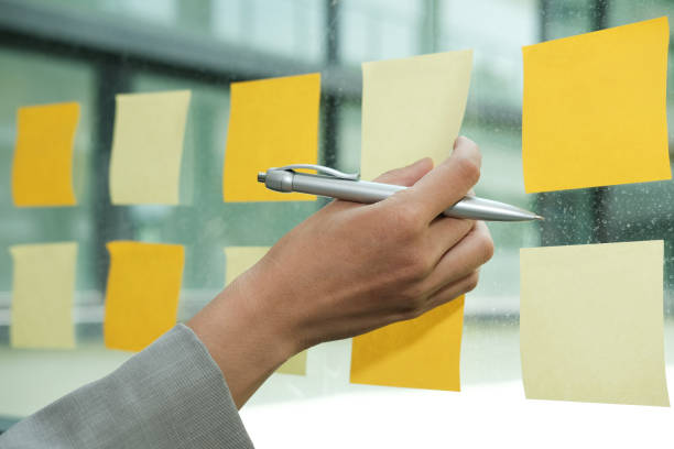 istock hand hold adhesive notes on glass wall. Sticky note paper reminder schedule for creative idea & business brainstorming 1058986274