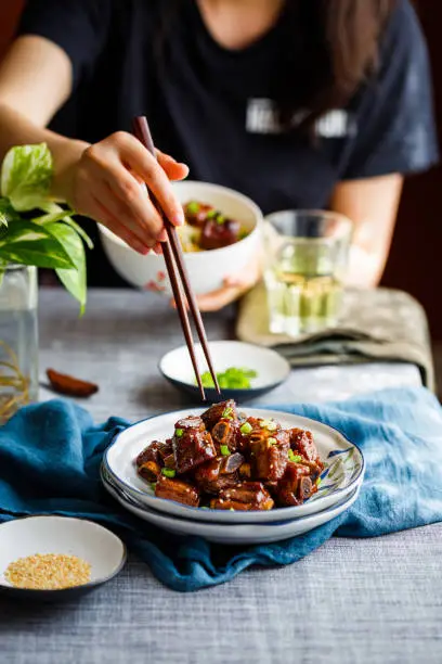 Young woman eating Chinese food sweet and sour pork ribs with chopsticks