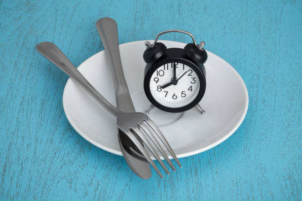 Intermittent fasting Intermittent fasting concept with clock on white plate, fork and knife on blue table fasting activity stock pictures, royalty-free photos & images