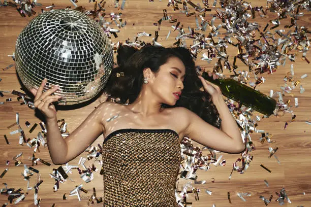 Beautiful young woman fell asleep on the floor with wine bottle and disco ball