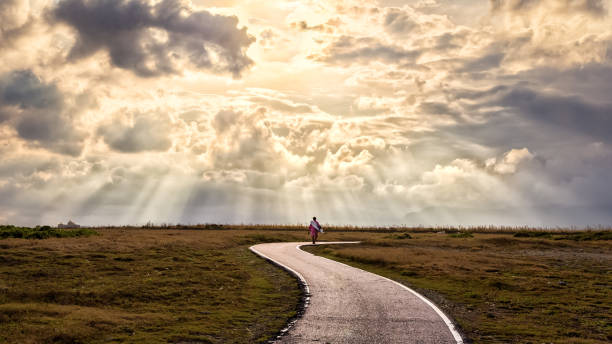 Concept image of a man walking along a path A person walking alone along s-shape path. The sun produces amazing light rays across the sky. The image is simple and breathtaking. This image is suitable for background use or add quote above. spiritual enlightenment stock pictures, royalty-free photos & images