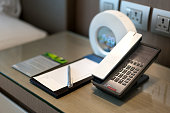 Black telephone and note in front and bed in the background, focus on the telephone,for room service,communication themes in hotel or resort.