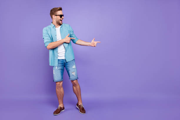 Full body size length of attractive bearded trendy stylish confident cheerful man, wearing denim and glasses, pointing with fingers aside, over bright violet purple background, empty blank copy space Full body size length of attractive bearded trendy stylish confident cheerful man, wearing denim and glasses, pointing with fingers aside, over bright violet purple background, empty blank copy space shorts stock pictures, royalty-free photos & images