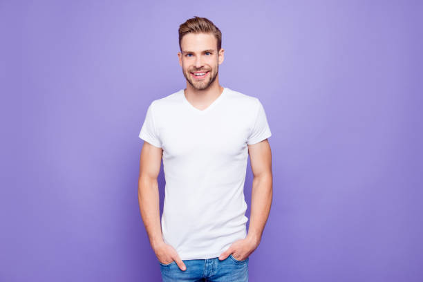 istock Handsome attractive bearded content guy in white tshirt and jeans with stubble, bristle keeping hands in pockets, isolated over bright vivid violet purple background 1059069074