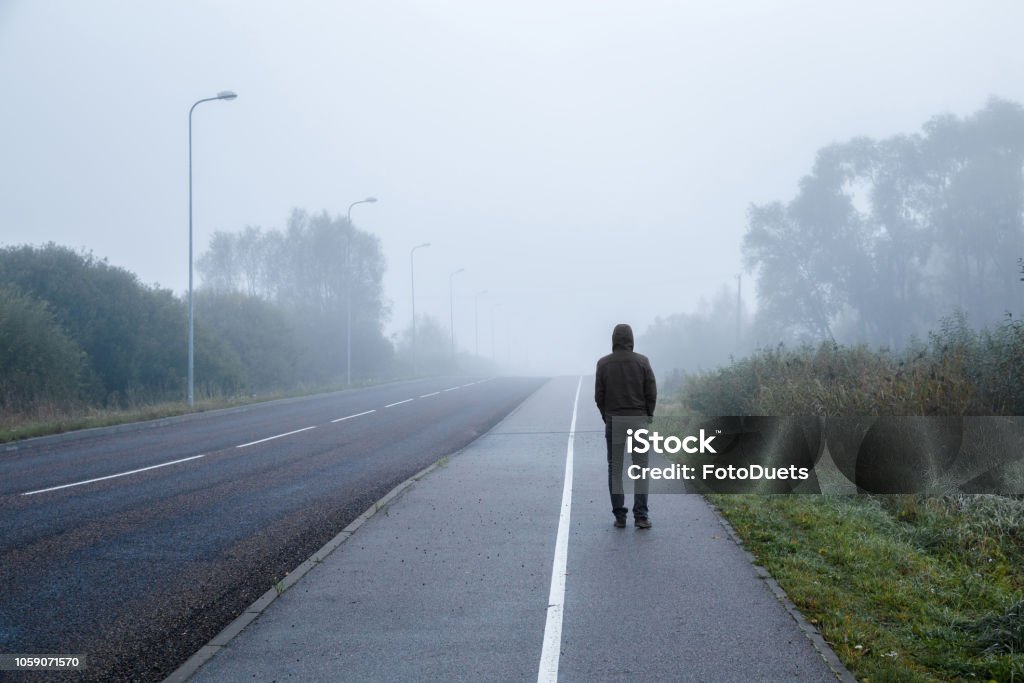 Young man alone walking on sidewalk in mist of early morning. Foggy air. Go away. Back view. Depression - Sadness Stock Photo