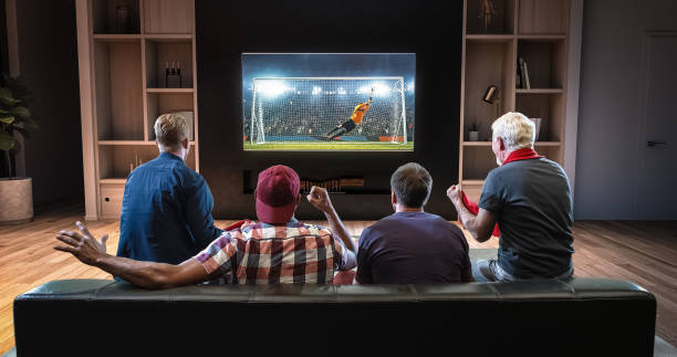 ファンのグループは、テレビ、リビング ルームのソファの上に座って、ゴールを祝ってサッカー瞬間を見ています。 - 観客 ストックフォトと画像
