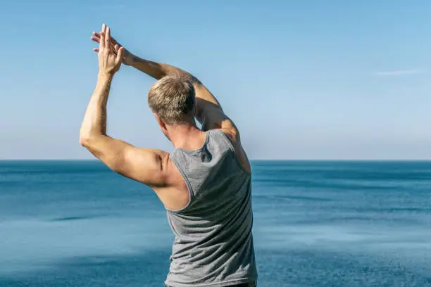 Photo of Man doing a warm-up exercise on the ocean. Fresh air and a healthy lifestyle