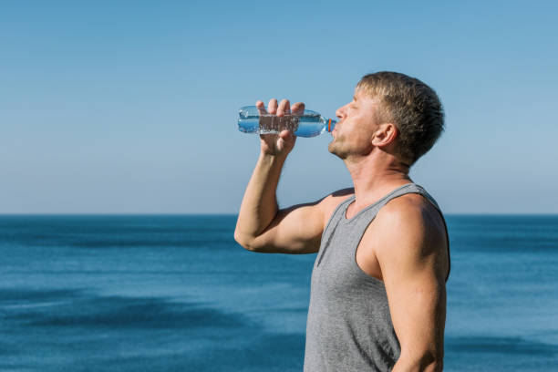 istock A man drinking and pours water on his face from bottle on the ocean, refreshing after a workout 1059077426