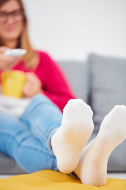 istock Girl holding TV remote and drinking coffee / tea on a couch. 1059080012