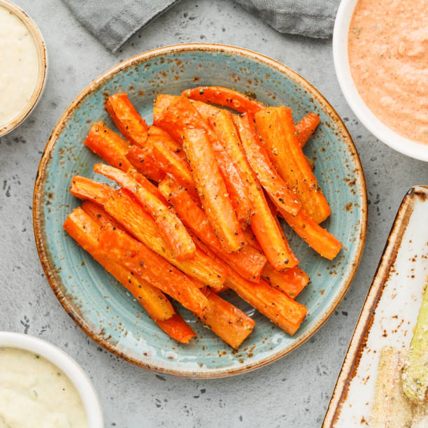 bastoncini di carota stagionati al forno con salsa e hummus. cibo vegetariano sano. lay piatto, vista dall'alto. - cooked roasted cooking fried foto e immagini stock