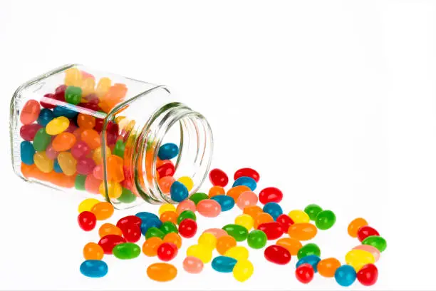 Photo of Jelly Beans candy spilled from glass jar isolated on white background
