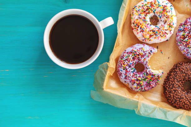 istock Delicious glazed donuts in box and cup of coffee on turquoise blue surface 1059089680
