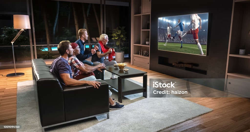 Grupo de fãs estão assistindo a um momento de futebol na TV e comemorando um gol, sentado no sofá na sala de estar. - Foto de stock de Televisor royalty-free