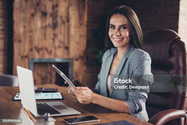 Foto Vista Lateral Del Jefe Inteligente Elegante En Una Chaqueta A Cuadros Gris Sentado En La Silla De La Oficina En La Estación De Trabajo En Estilo Industrial Media Vuelta Con Una Tableta En La Mano Foto de stock y más banco de imágenes de Mujeres