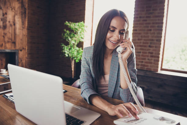 Smart, clever and intelligent agent lady in gray checkered blazer dials a phone number to contact the delivery department and send the order to customer Smart, clever and intelligent agent lady in gray checkered blazer dials a phone number to contact the delivery department and send the order to customer landline phone stock pictures, royalty-free photos & images