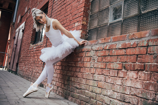 beautiful young ballerina leaning at brick wall and looking away