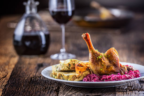 Portion of roast duck leg red cabbage homemade dumplings on plate and red wine on the background. Portion of roast duck leg red cabbage homemade dumplings on plate and red wine on the background. confit stock pictures, royalty-free photos & images