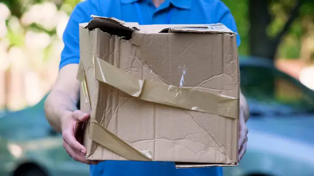 Photo of Male courier showing damaged box, cheap parcel delivery, poor shipment quality