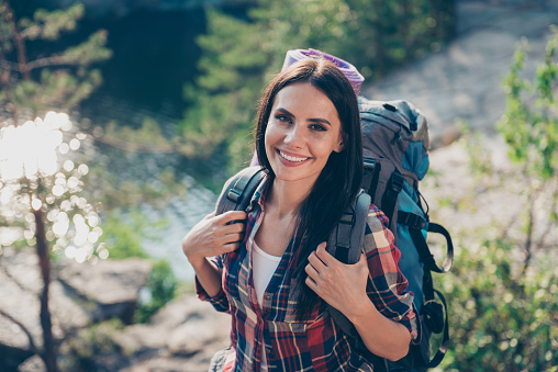 Portrait of adorable beautiful nice lovely cute cheerful long-haired girl, wearing casual checkered shirt, backpacking, wandering, exploring the world. Spending spare time in wild wood