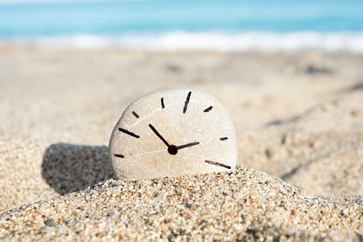clock drawn on a stone, on the sand of a beach
