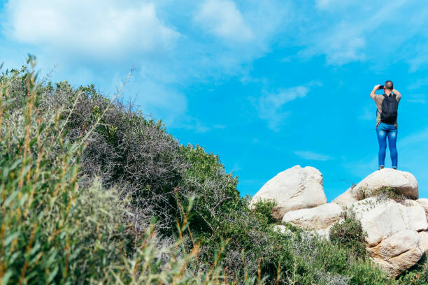 man taking a photo in Corsica, France a young caucasian man, seen from behind, on the top of a rock formation taking a photo of the landscape in the Sout of Corsica, in France, with his smartphone 7944 stock pictures, royalty-free photos & images