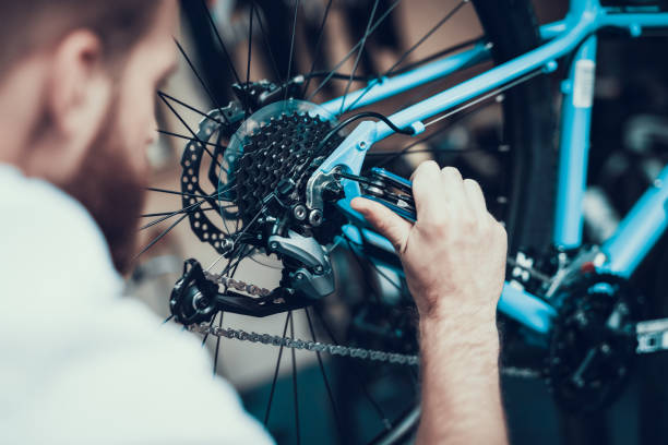 Bike Mechanic Repairs Bicycle in Workshop Bike Mechanic Repairs Bicycle in Workshop. Closeup Portrait of Young Blurred Man Examines and Fixes Modern Cycle Transmission System. Bike Maintenance and Sport Shop Concept bicycle shop stock pictures, royalty-free photos & images