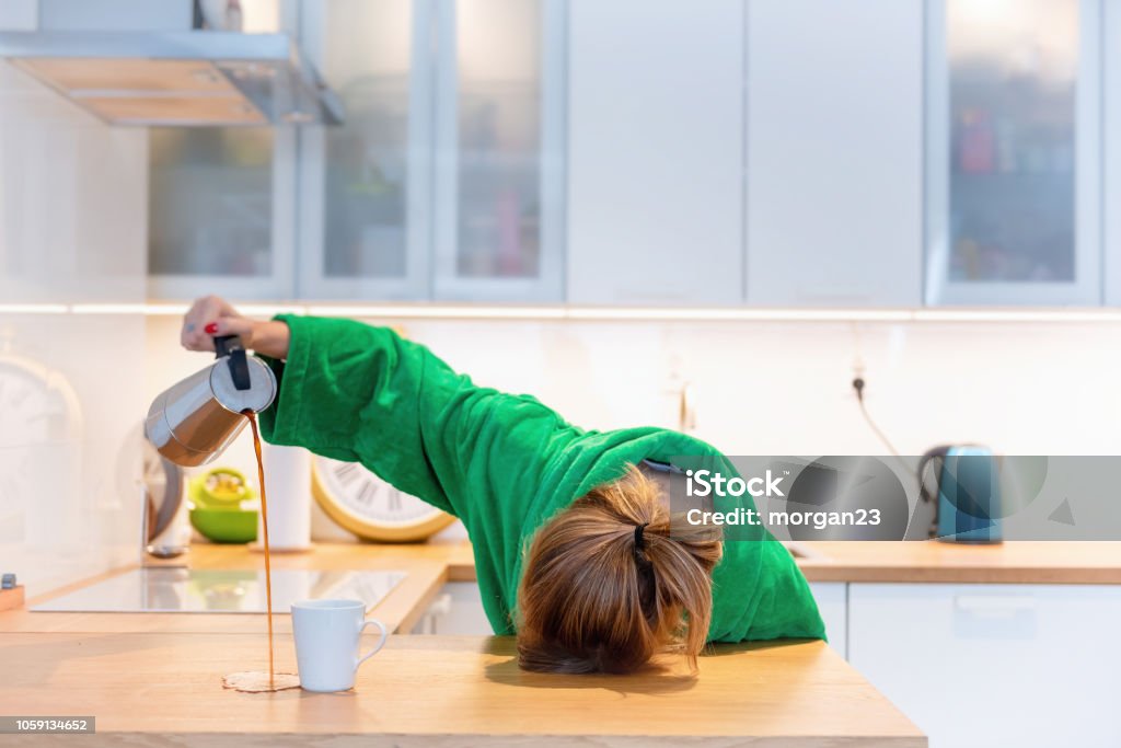 Fatigué femme allongée sur la table de la cuisine au petit déjeuner. Essayer de boire du café du matin - Photo de Fatigué libre de droits