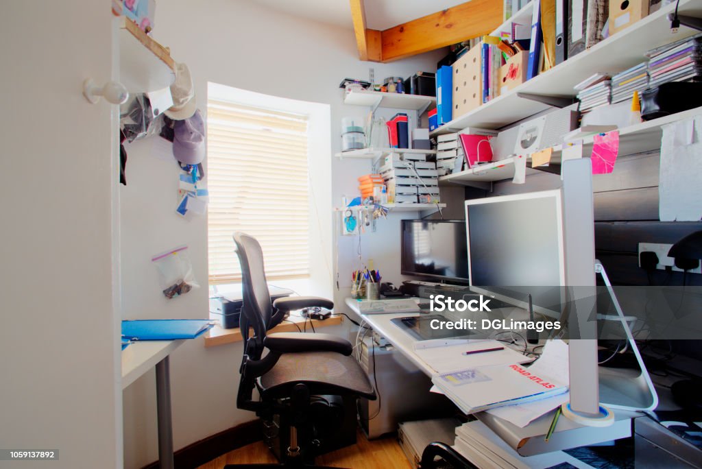 Home Office A shot of a messy desk in a home office, the room is small and cluttered, on the desk is three computer monitors and office supplies. Messy Stock Photo