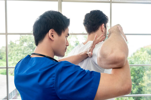 fisioterapeuta que estira el brazo y hombro paciente varón atleta - massaging men swedish culture male fotografías e imágenes de stock