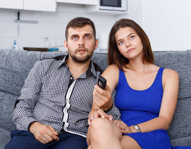 istock Smiling young couple sitting on sofa at home watching TV 1059142564