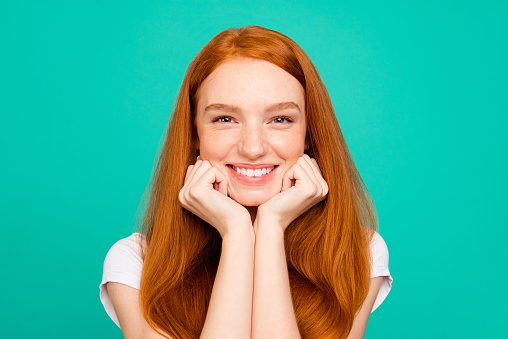 Portrait of nice calm positive cheerful cute bright vivid shiny red straight-haired girl in casual white t-shirt, holding chin with fists, isolated over turquoise green background