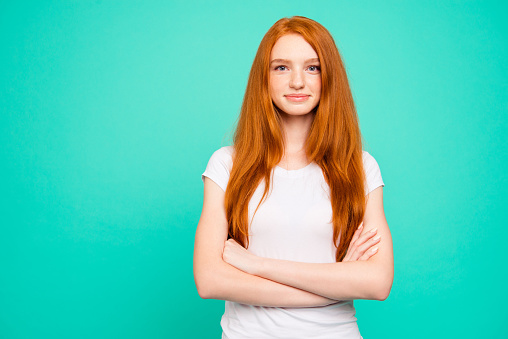 Portrait of nice calm content positive peaceful cute bright vivid shiny red straight-haired girl in casual white t-shirt, folded hands, isolated over turquoise green background