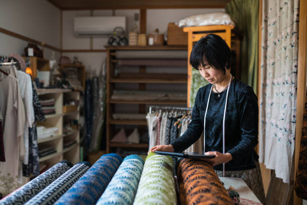 femme mûre en utilisant une tablette numérique à dresser l’inventaire des produits textiles finis qu'elle a conçu - arts and crafts movement photos et images de collection