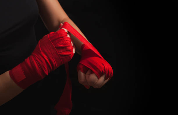 Female boxer is wrapping hands with red boxing wraps. Isolated on black background with copy space. Strong hand and ready for fight, active exercise and sparring. Close up. Women self defense.