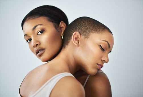 Studio shot of two beautiful young women embracing each other against a gray background