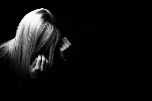 Depressed woman hiding her face in a dark stock photo