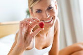 Beautiful young woman showing a raspberry and looking at camera in the bedroom.